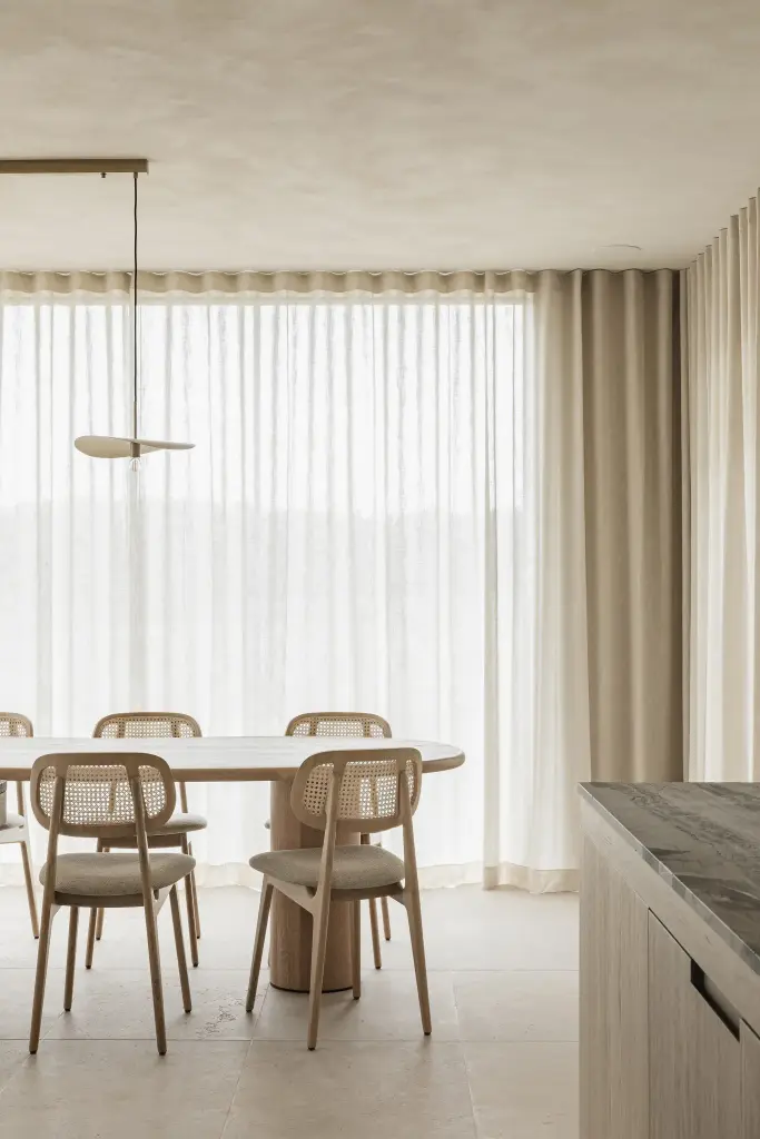 Rotan eetstoelen aan de ovale eiken tafel voor het gordijn, where architecture creates space for experience, interieur Laura Calleeuw