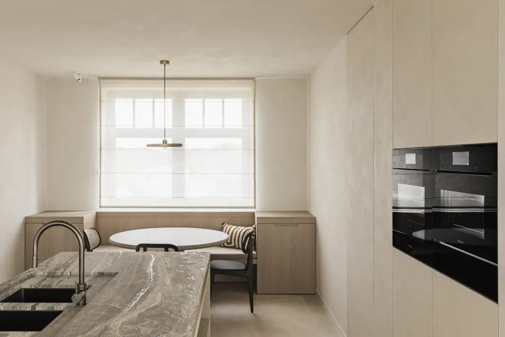 Keuken met travertijn eiland, inbouwovens en eethoek met zitbank onder het raam, where architecture creates space for experience, interieur Laura Calleeuw