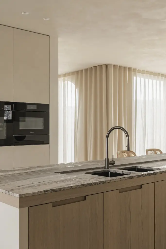 Keuken met travertijn eiland, inbouwovens en eethoek met zitbank onder het raam, where architecture creates space for experience, interieur Laura Calleeuw