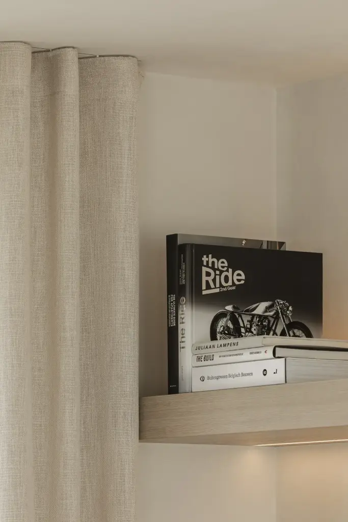 Verlichte plank met boeken naast een linnen gordijn, where architecture creates space for experience, interieur Laura Calleeuw