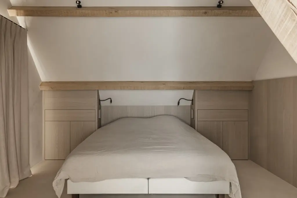Slaapkamer onder het dak met eikenhouten balk, bed en leeslampjes, where architecture creates space for experience, interieur Laura Calleeuw