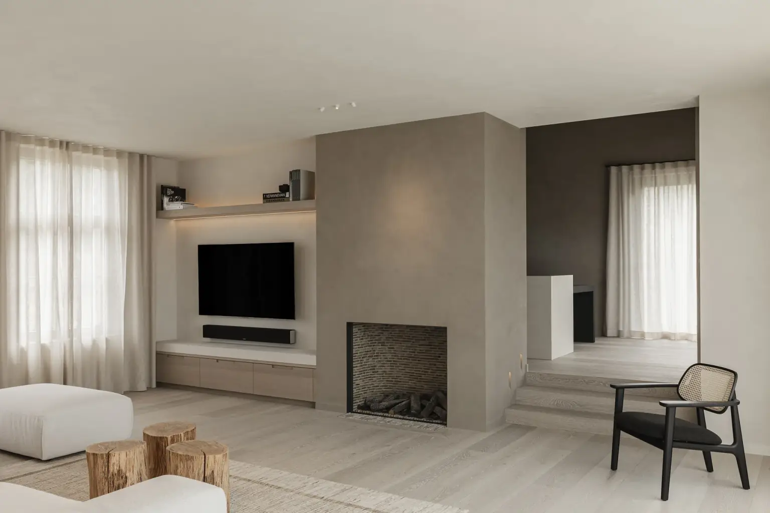 Woonkamer met gashaard in microcement schouw, televisiewand en rotan fauteuil, where architecture creates space for experience, interieur Laura Calleeuw