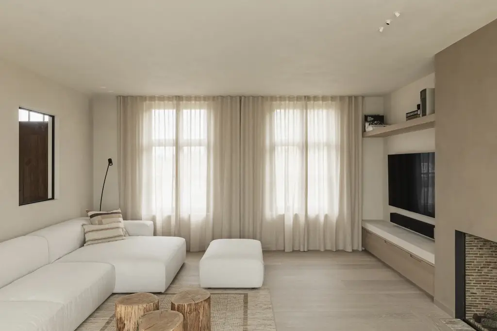 Woonkamer met witte hoekzetel, boomstamtafeltjes en hoge ramen met gordijnen, where architecture creates space for experience, interieur Laura Calleeuw