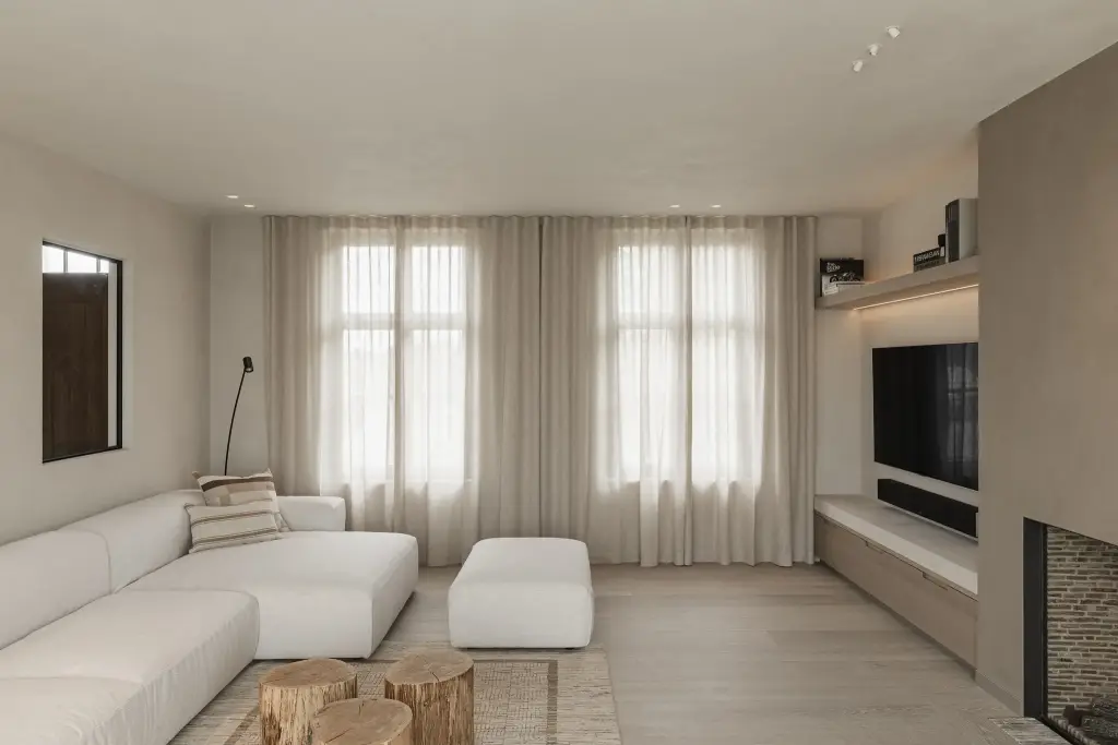 Woonkamer met witte hoekzetel, boomstamtafeltjes en hoge ramen met gordijnen, where architecture creates space for experience, interieur Laura Calleeuw