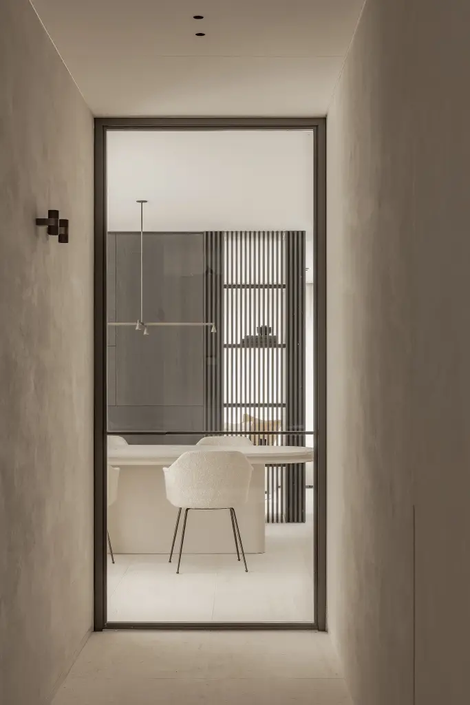 Doorkijk naar de eetruimte door een stalen deur in een microcement gang, Kijkwoning in Erpe-Mere, interieur Laura Calleeuw