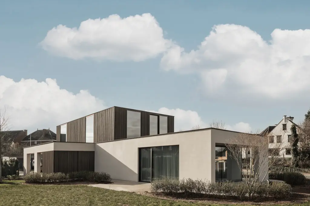 Moderne gevel van het gebouw met donkere houten lamellen en lichte crepi, met drie vlaggen aan de straatkant, Kijkwoning in Erpe-Mere, interieur Laura Calleeuw