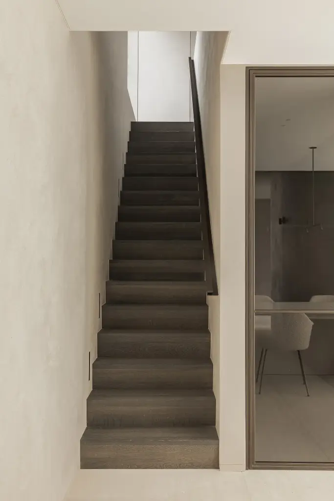 Trap met donkere eiken treden tussen microcement wanden, Kijkwoning in Erpe-Mere, interieur Laura Calleeuw