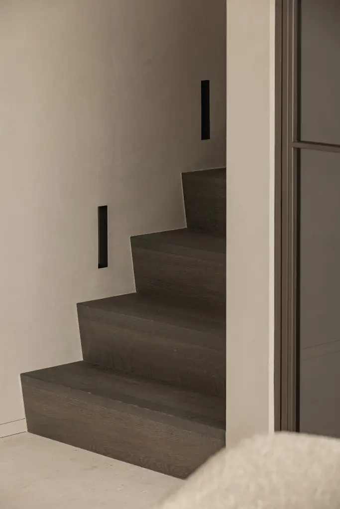 Trap met donkere eiken treden tussen microcement wanden, Kijkwoning in Erpe-Mere, interieur Laura Calleeuw