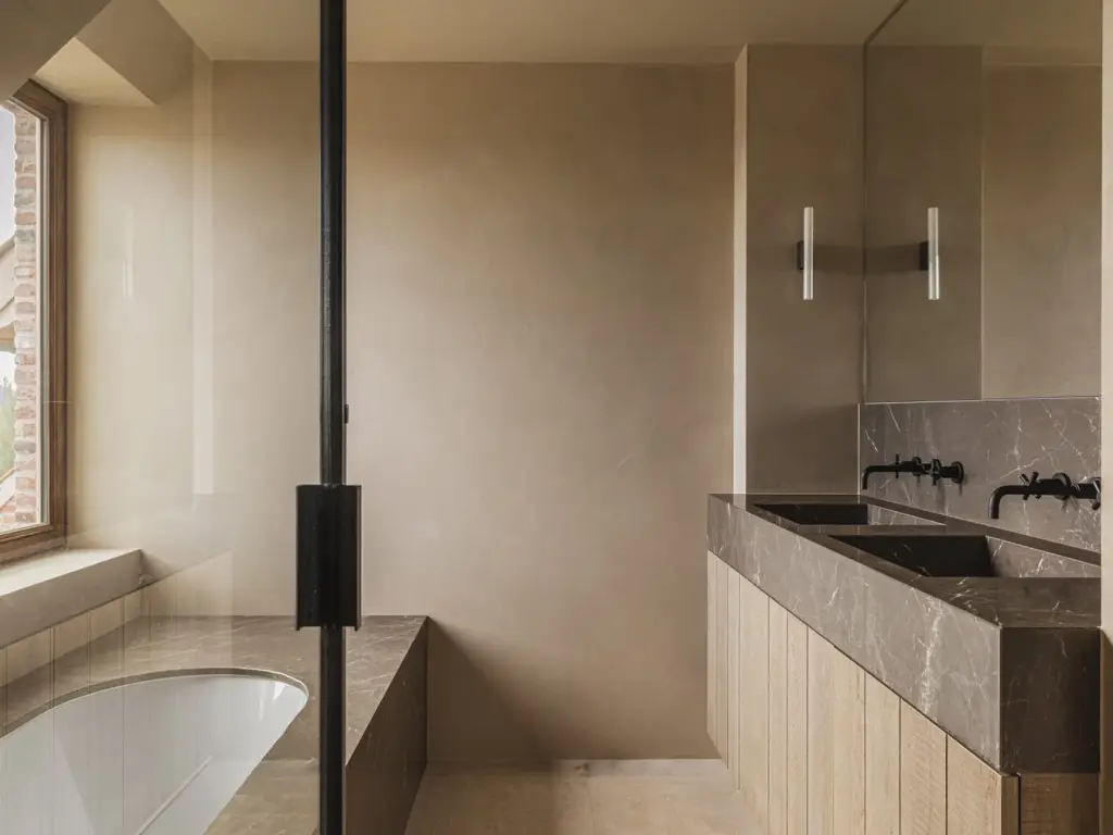 Badkamer met dubbele wastafel in natuursteen, ligbad, raam en stalen glaswand, Landelijke woning in Torhout, interieur Laura Calleeuw