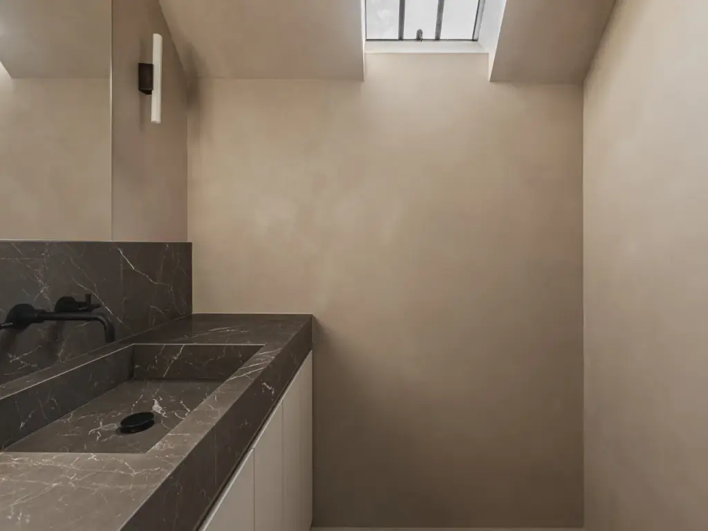 Badkamer met wastafel in donker natuursteen, zwarte wandkranen, kalkpleisterwanden en dakraam, Landelijke woning in Torhout, interieur Laura Calleeuw