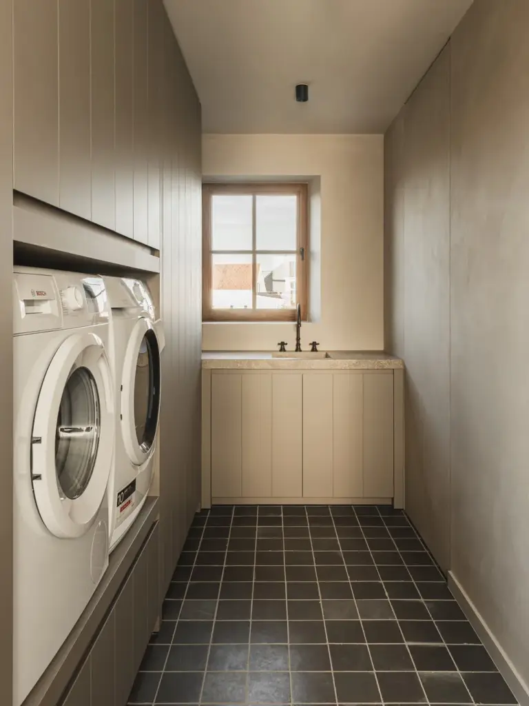 Bijkeuken met wasmachine en droogkast, houten kasten en een donkere tegelvloer, Landelijke woning in Torhout, interieur Laura Calleeuw