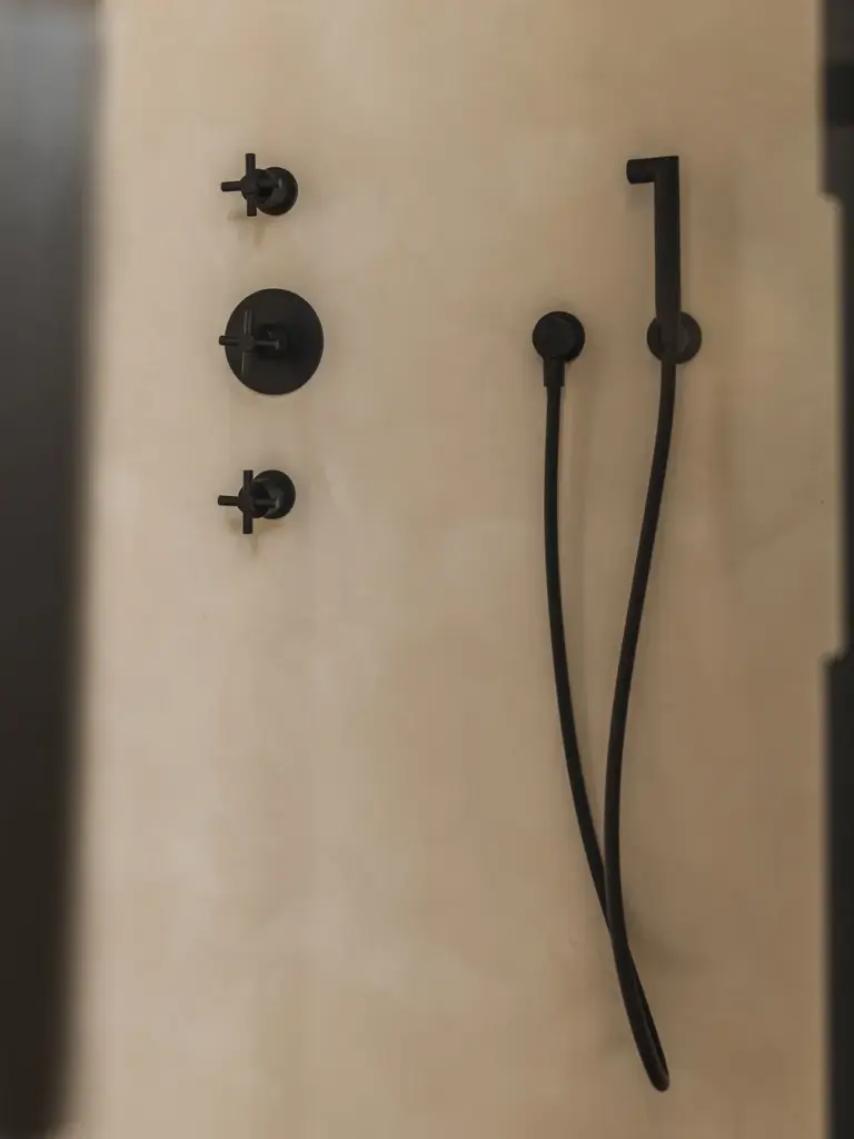 Zwarte handdouche en thermostaatkranen op een kalkpleisterwand, Landelijke woning in Torhout, interieur Laura Calleeuw