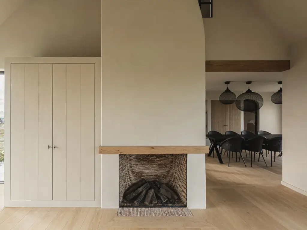 Woonruimte met open haard in een gepleisterde schouw met eikenhouten balk, kast en eethoek met hanglampen, Landelijke woning in Torhout, interieur Laura Calleeuw