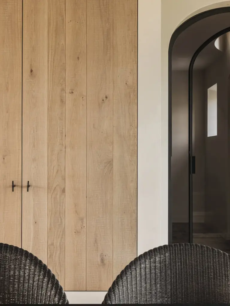 Eikenhouten kast met verticale planken naast een zwarte stalen deur en rieten stoelen, Landelijke woning in Torhout, interieur Laura Calleeuw