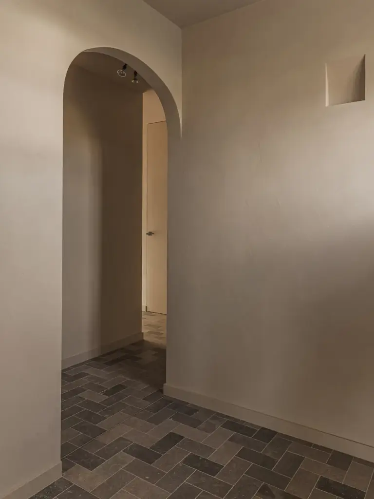 Gang met boogopeningen in kalkpleister en een vloer van klinkers, Landelijke woning in Torhout, interieur Laura Calleeuw