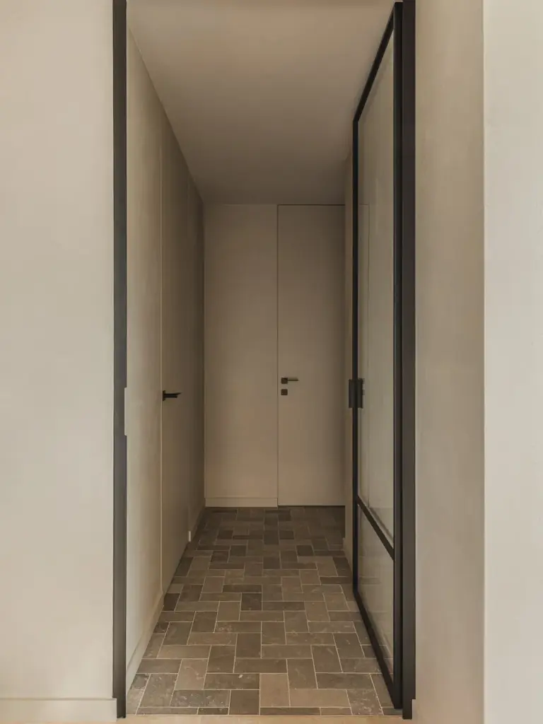 Gang met stalen glasdeur, vlakke deuren en een vloer van klinkers, Landelijke woning in Torhout, interieur Laura Calleeuw