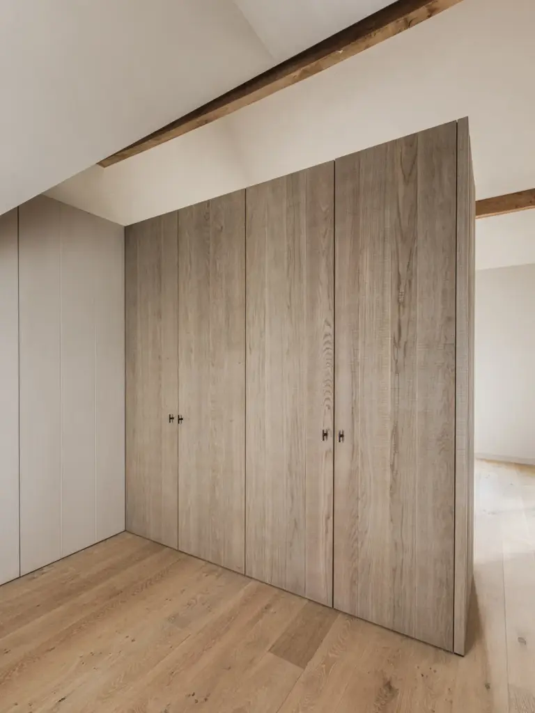 Kastenwand in gebeitst eiken onder de dakhelling met een zichtbare houten balk, Landelijke woning in Torhout, interieur Laura Calleeuw