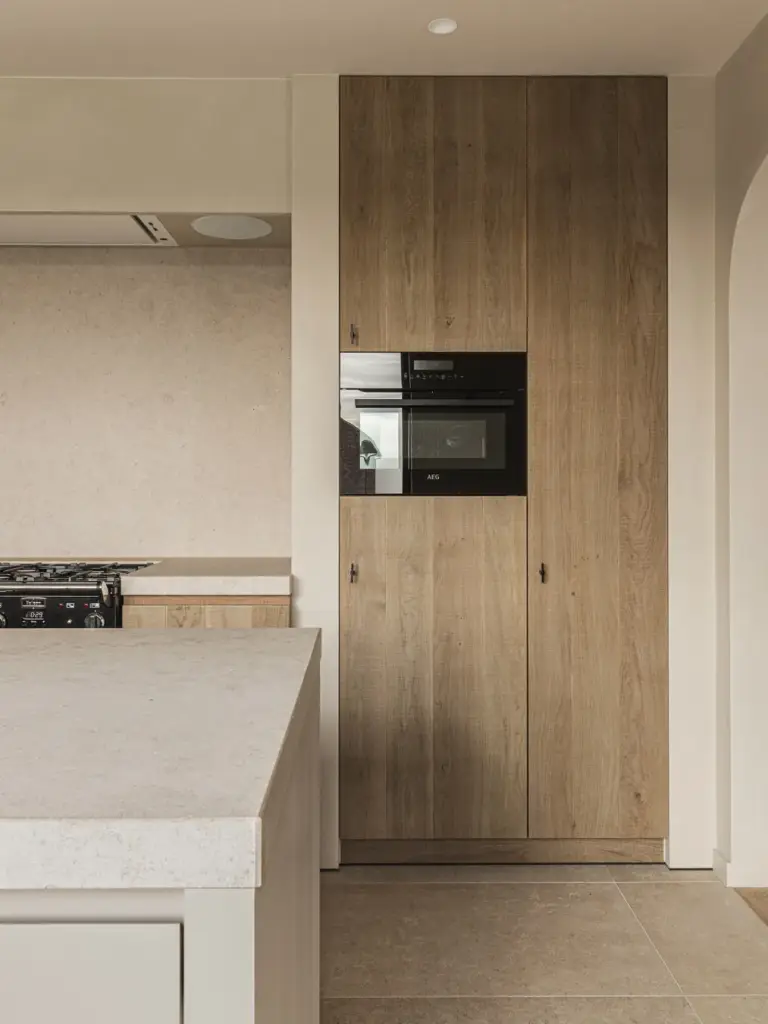 Eikenhouten kast met inbouwoven naast het natuurstenen kookeiland, Landelijke woning in Torhout, interieur Laura Calleeuw