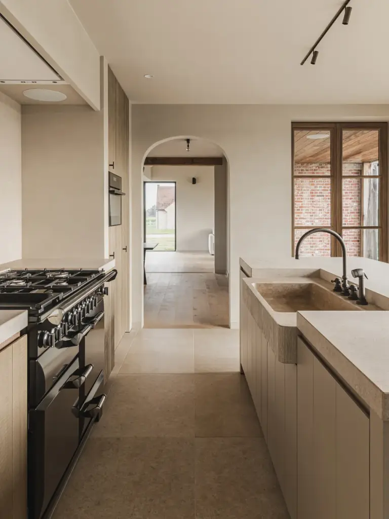 Keuken met fornuis en spoelbak in natuursteen met doorkijk naar de veranda, Landelijke woning in Torhout, interieur Laura Calleeuw