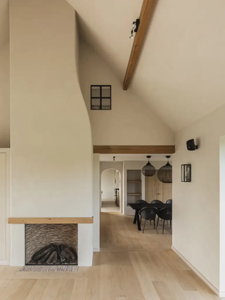 Open haard met schouw onder de schuine dakbalken en doorkijk naar de eethoek, Landelijke woning in Torhout, interieur Laura Calleeuw