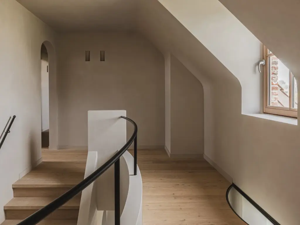 Overloop met gebogen trapleuning in zwart, eikenhouten treden, boogdeur en een raam in de dakhelling, Landelijke woning in Torhout, interieur Laura Calleeuw