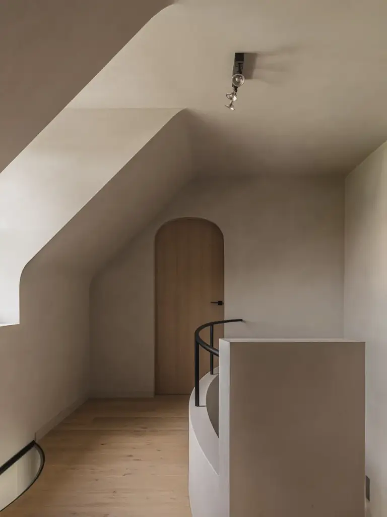 Overloop met gebogen trapleuning in zwart, eikenhouten treden, boogdeur en een raam in de dakhelling, Landelijke woning in Torhout, interieur Laura Calleeuw
