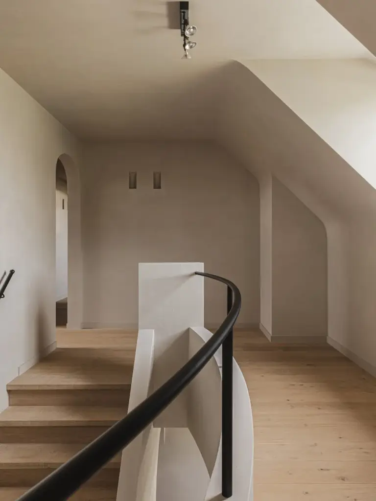 Overloop met gebogen trapleuning in zwart, eikenhouten treden, boogdeur en een raam in de dakhelling, Landelijke woning in Torhout, interieur Laura Calleeuw