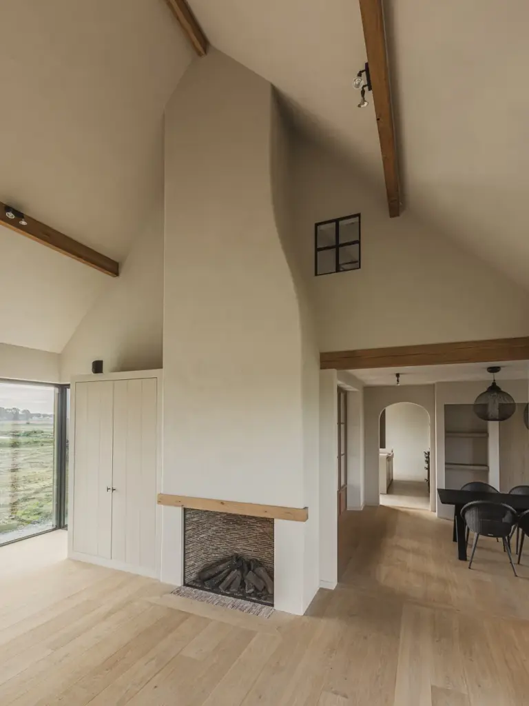 Gepleisterde schouw met bakstenen haard onder houten balken, met zicht op de eethoek, Landelijke woning in Torhout, interieur Laura Calleeuw