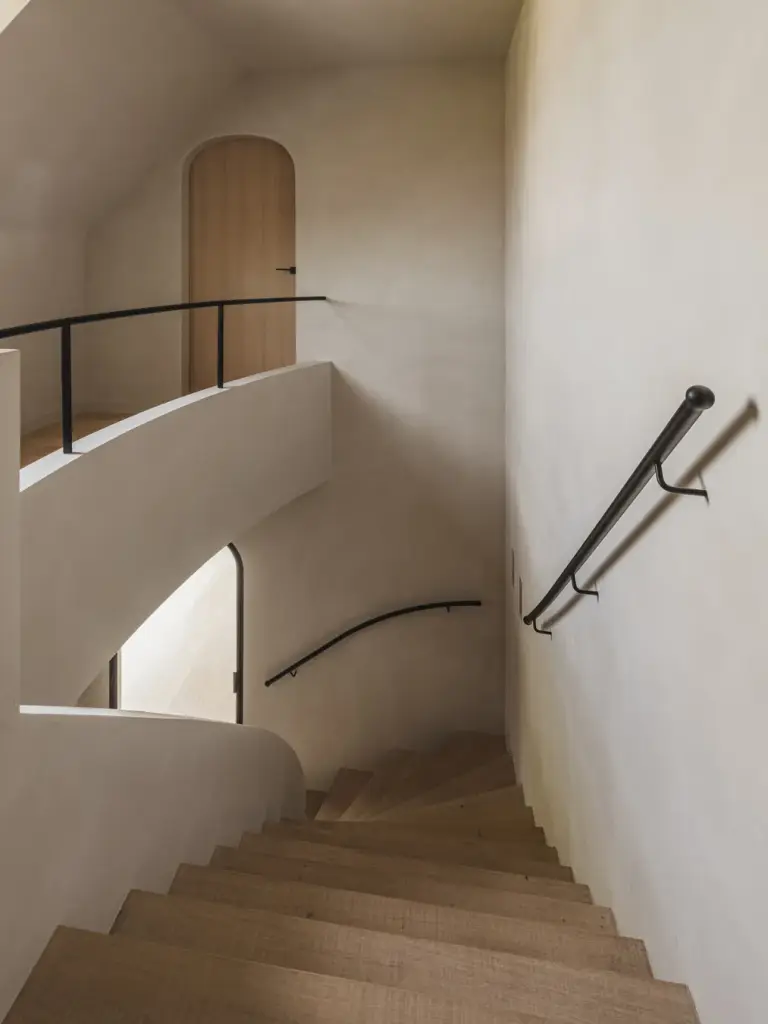Trappenhuis met houten boogdeur, gebogen gepleisterde leuning en zwarte handgreep, Landelijke woning in Torhout, interieur Laura Calleeuw