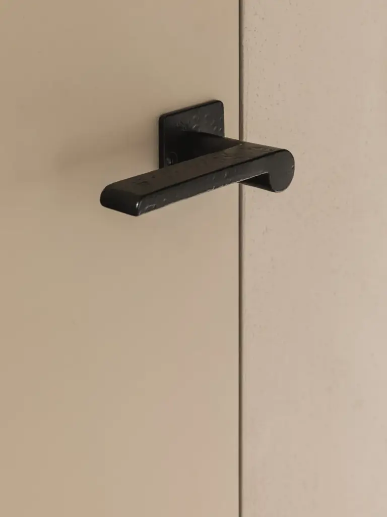 Detail van een zwarte deurklink op een vlakke deur, Landelijke woning in Torhout, interieur Laura Calleeuw