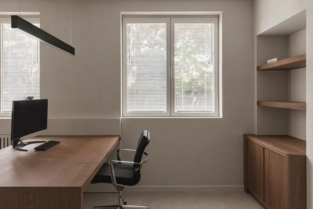 Werkkamer met eiken bureau, lange lamp, bureaustoel en een nis met planken boven een eiken kast, Herenhuis in Roeselare, interieur Laura Calleeuw