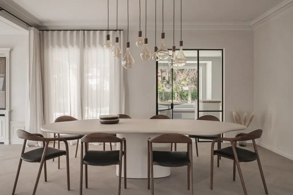 Eetkamer met lange ovale tafel, zes stoelen, een reeks hanglampen en een stalen glasdeur naar de tuin, Herenhuis in Roeselare, interieur Laura Calleeuw