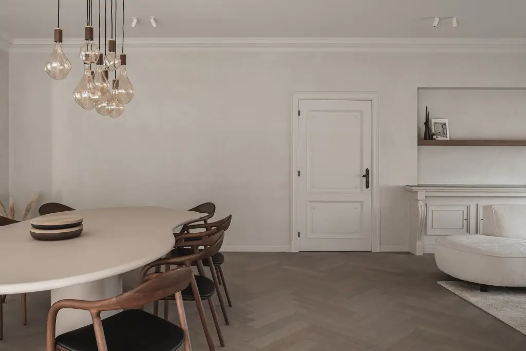 Eetkamer met ovale tafel, houten stoelen, hanglampen met gloeilampen en een witte paneeldeur, Herenhuis in Roeselare, interieur Laura Calleeuw