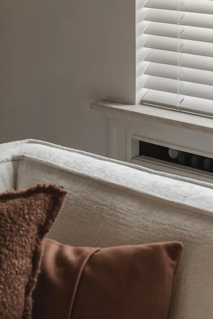 Detail van een kussen op de sofa bij een radiator onder een jaloezie, Herenhuis in Roeselare, interieur Laura Calleeuw