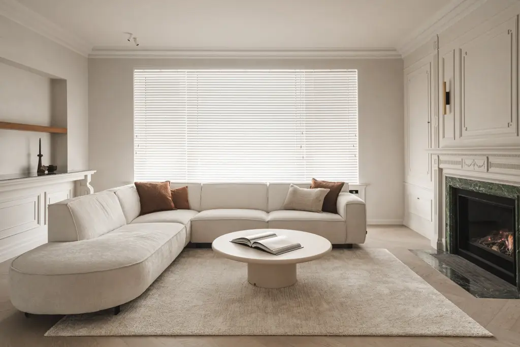 Woonkamer met hoeksofa, ronde salontafel, open haard met groen marmer en klassieke lambrisering, Herenhuis in Roeselare, interieur Laura Calleeuw
