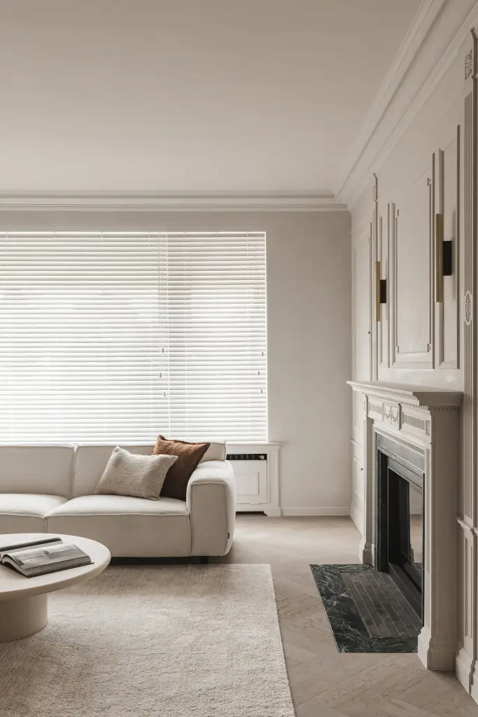 Woonkamer met sofa, ronde salontafel en open haard in groen marmer voor een raam met jaloezie, Herenhuis in Roeselare, interieur Laura Calleeuw