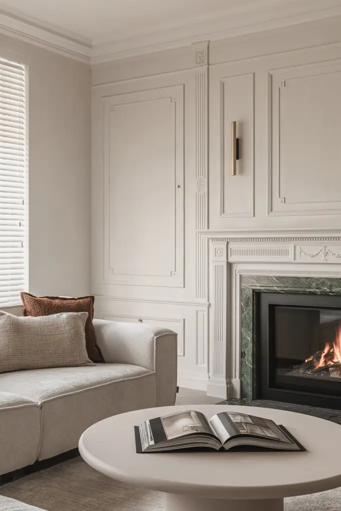 Hoek van de woonkamer met sofa, salontafel, open haard en lambrisering, Herenhuis in Roeselare, interieur Laura Calleeuw