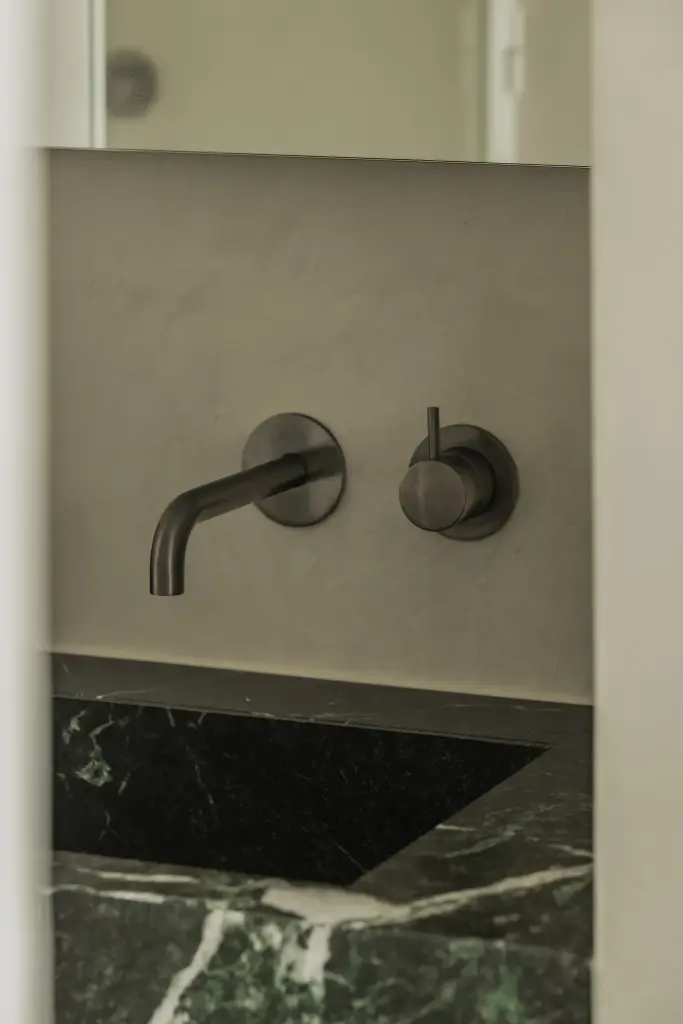 Wandkranen boven een wastafel in groen marmer en microcement wand, Compact appartement in Knokke, interieur Laura Calleeuw