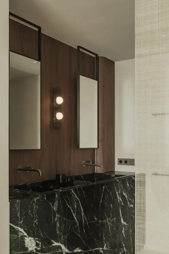 Badkamer met wastafel in groen marmer, smalle spiegels en wandlamp, Compact appartement in Knokke, interieur Laura Calleeuw