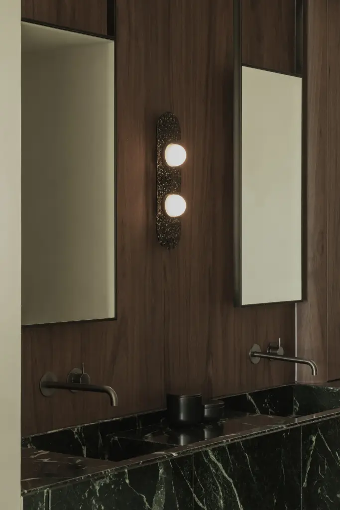 Badkamer met wastafel in groen marmer, smalle spiegels en wandlamp, Compact appartement in Knokke, interieur Laura Calleeuw