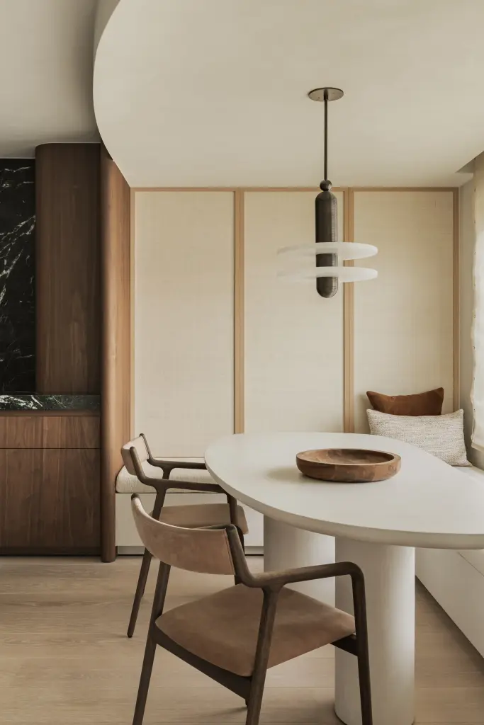 Eethoek met ovale tafel, leren stoelen, hanglamp en zitbank onder het raam, Compact appartement in Knokke, interieur Laura Calleeuw