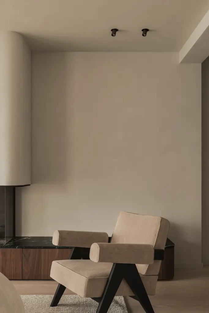 Twee fauteuils met zwarte poten naast de ronde haardschouw, Compact appartement in Knokke, interieur Laura Calleeuw