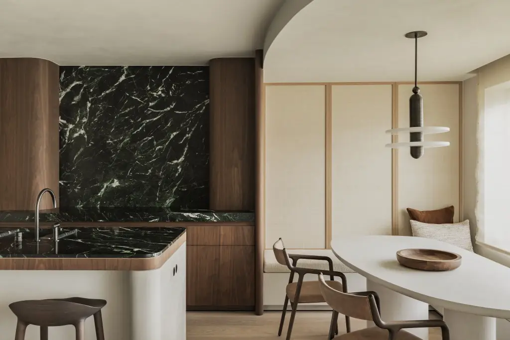 Keuken met marmeren achterwand, eiland, ovale eettafel en zitbank, Compact appartement in Knokke, interieur Laura Calleeuw