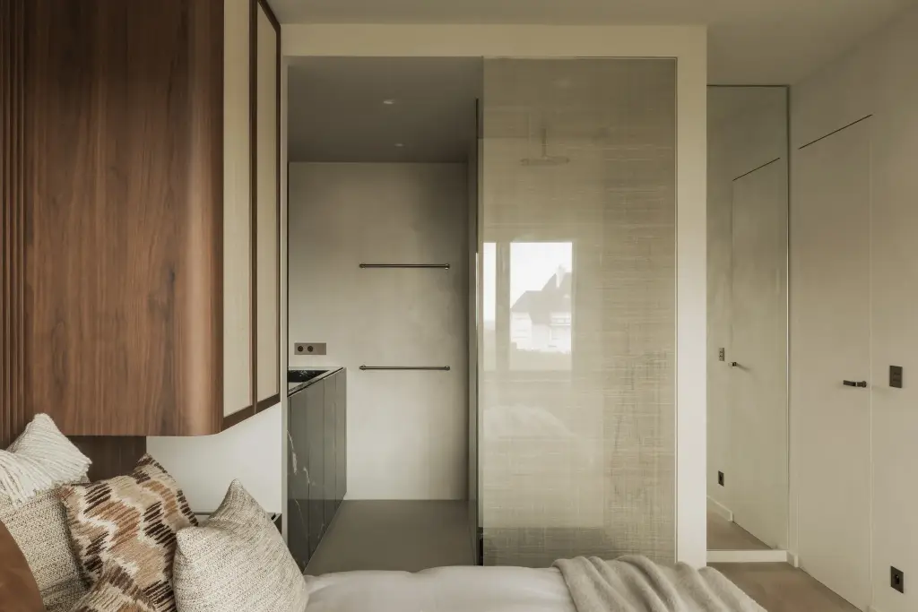 Slaapkamer met doorkijk naar de badkamer achter een rieten glaswand, Compact appartement in Knokke, interieur Laura Calleeuw