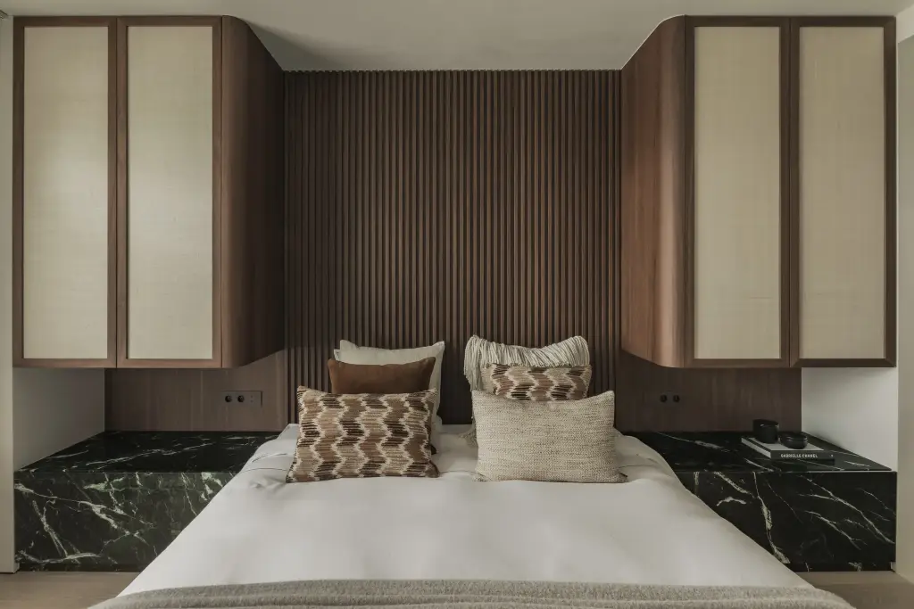 Slaapkamer met bed tussen nachtkastjes in groen marmer en kasten met rieten panelen, Compact appartement in Knokke, interieur Laura Calleeuw