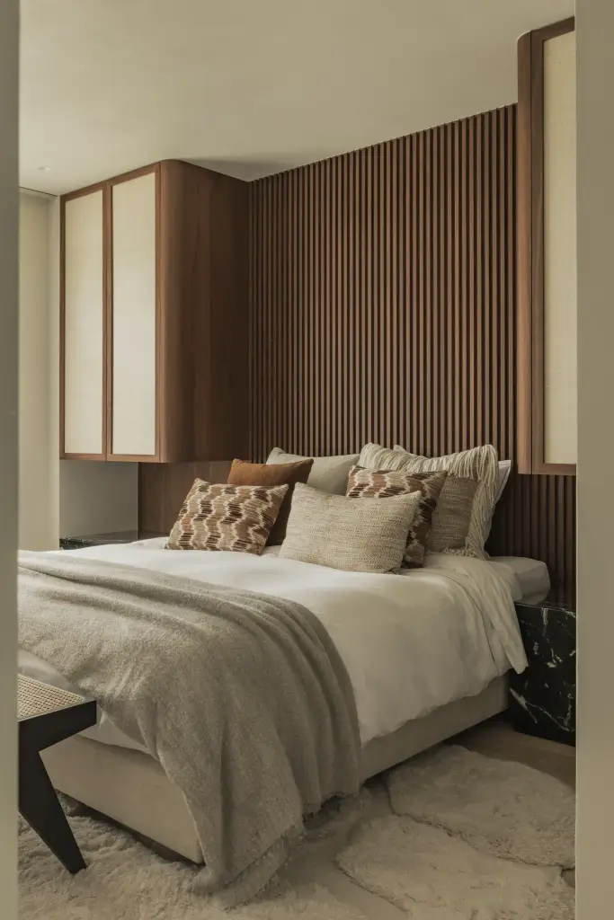 Slaapkamer met bed, lamellenwand in walnoot, plaid en wollen tapijt, Compact appartement in Knokke, interieur Laura Calleeuw