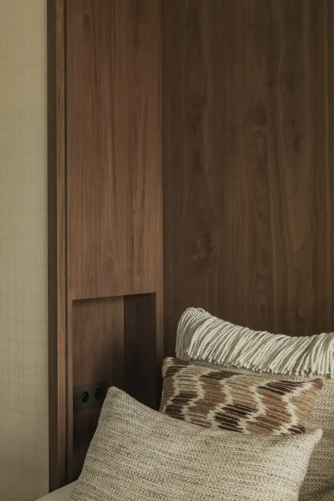 Detail van het bed in de walnoten nis met sierkussens en inbouwstopcontact, Compact appartement in Knokke, interieur Laura Calleeuw