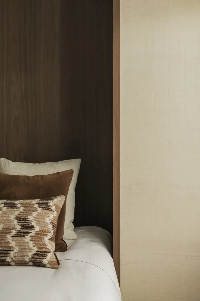 Detail van het bed in de walnoten nis met sierkussens en inbouwstopcontact, Compact appartement in Knokke, interieur Laura Calleeuw