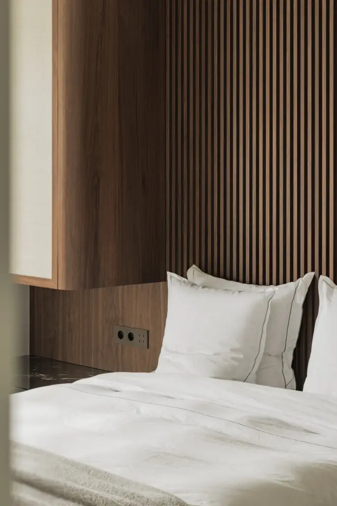 Slaapkamer met bed voor een walnoten lamellenwand en kasten met rieten panelen, Compact appartement in Knokke, interieur Laura Calleeuw