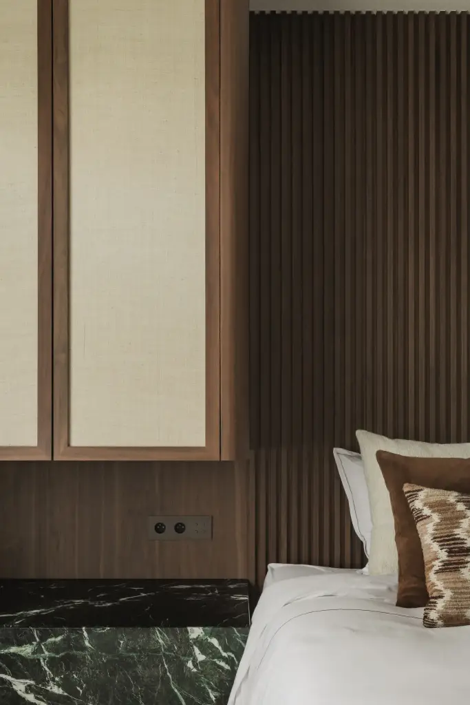 Slaapkamer met bed voor een walnoten lamellenwand en kasten met rieten panelen, Compact appartement in Knokke, interieur Laura Calleeuw
